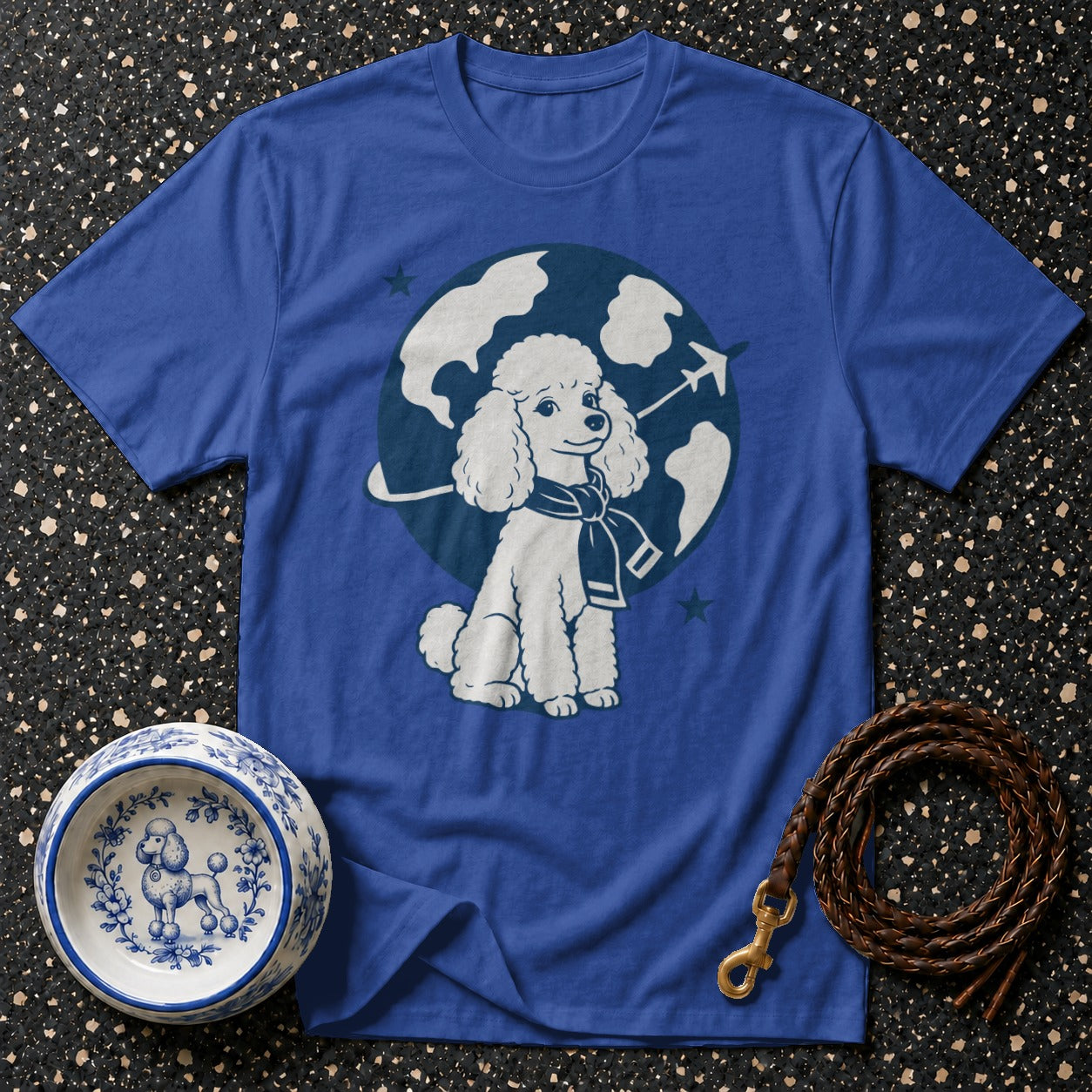 Blue t-shirt with a white poodle graphic wearing a scarf in front of a globe and airplane.