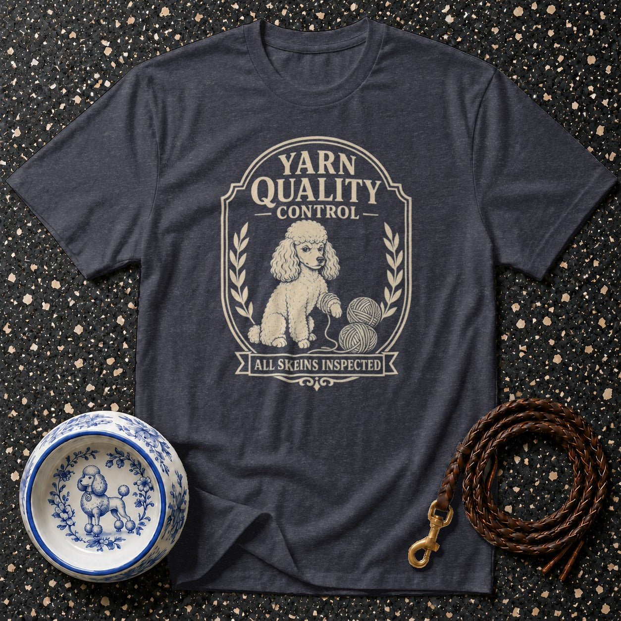 Dark t-shirt with a cream graphic of a poodle inspecting yarn skeins.