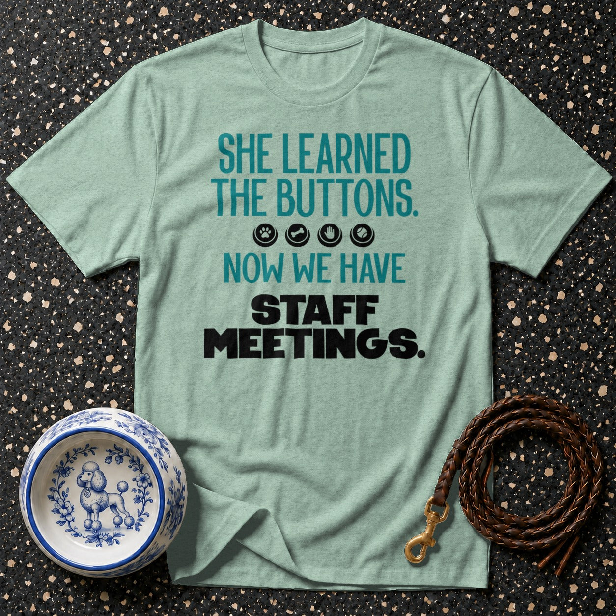 T-shirt with teal text: "SHE LEARNED THE BUTTONS. NOW WE HAVE STAFF MEETINGS."