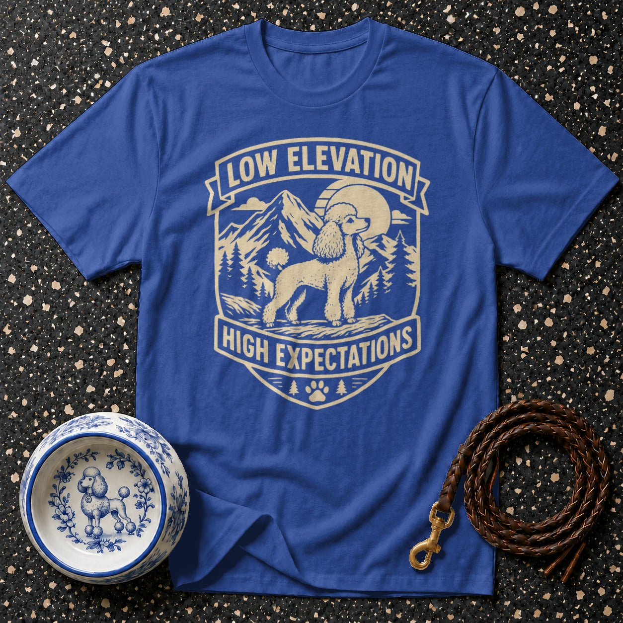 Blue t-shirt with a graphic featuring a poodle, mountains, and the text "Low Elevation High Expectations".