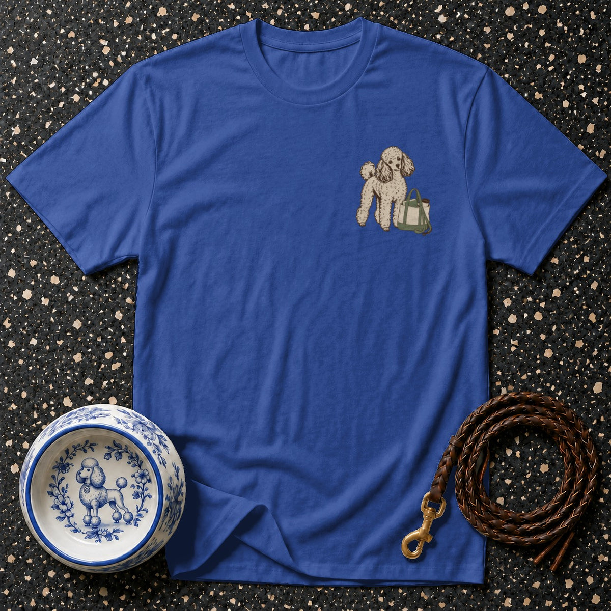 Blue t-shirt with embroidered poodle and green bag on chest pocket area.