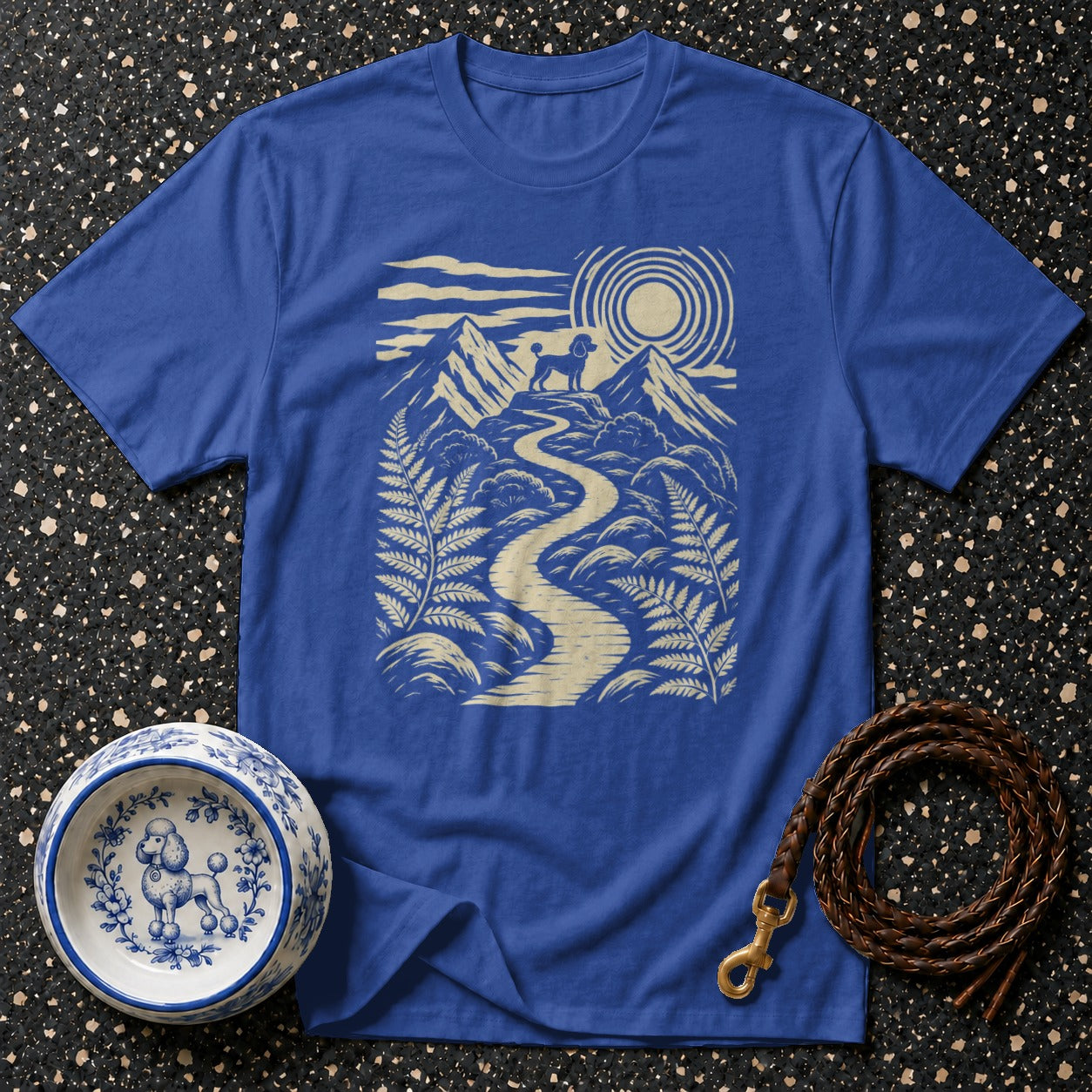 Blue t-shirt with beige graphic of poodle on mountain path.