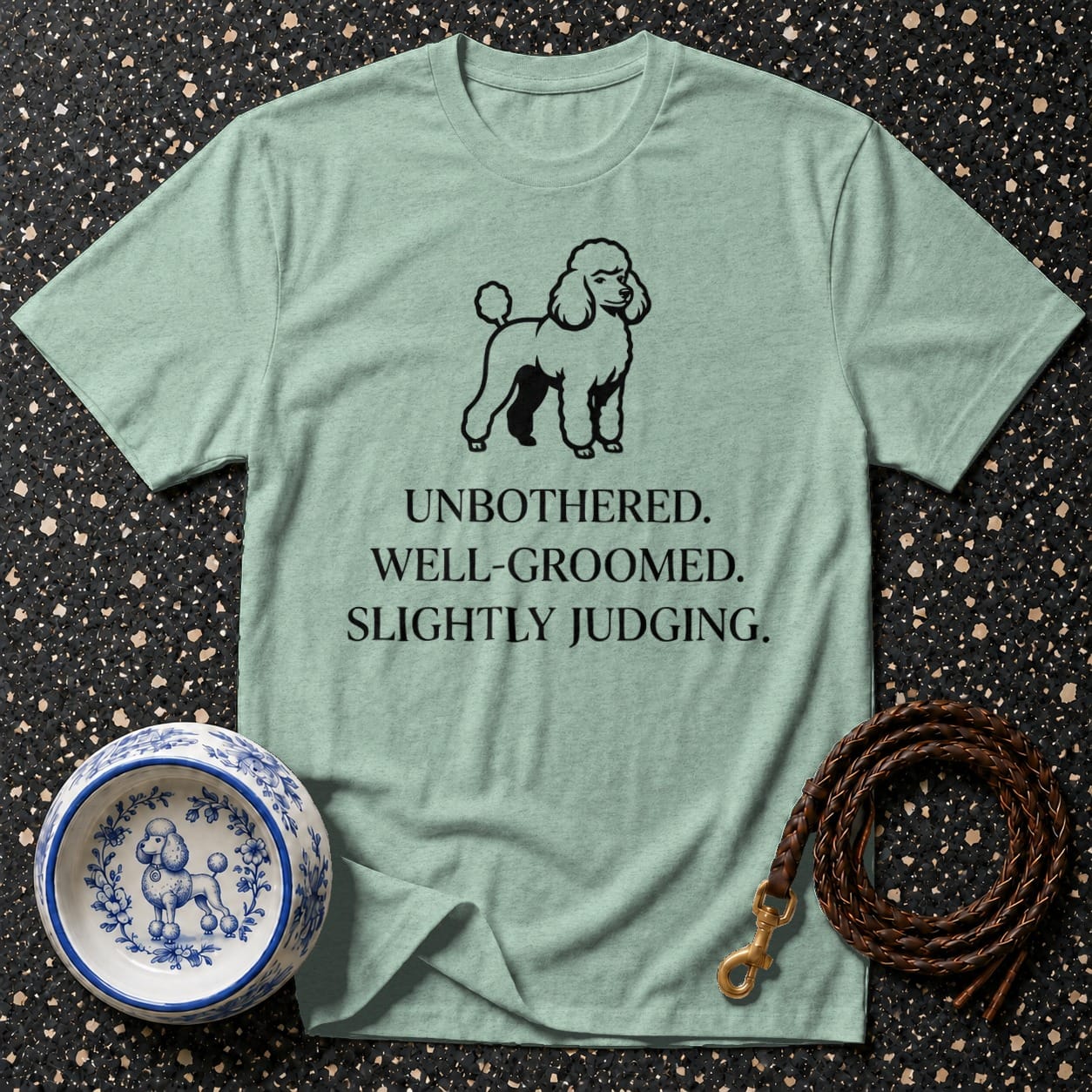 Light teal t-shirt with poodle graphic and text: UNBOTHERED. WELL-GROOMED. SLIGHTLY JUDGING.