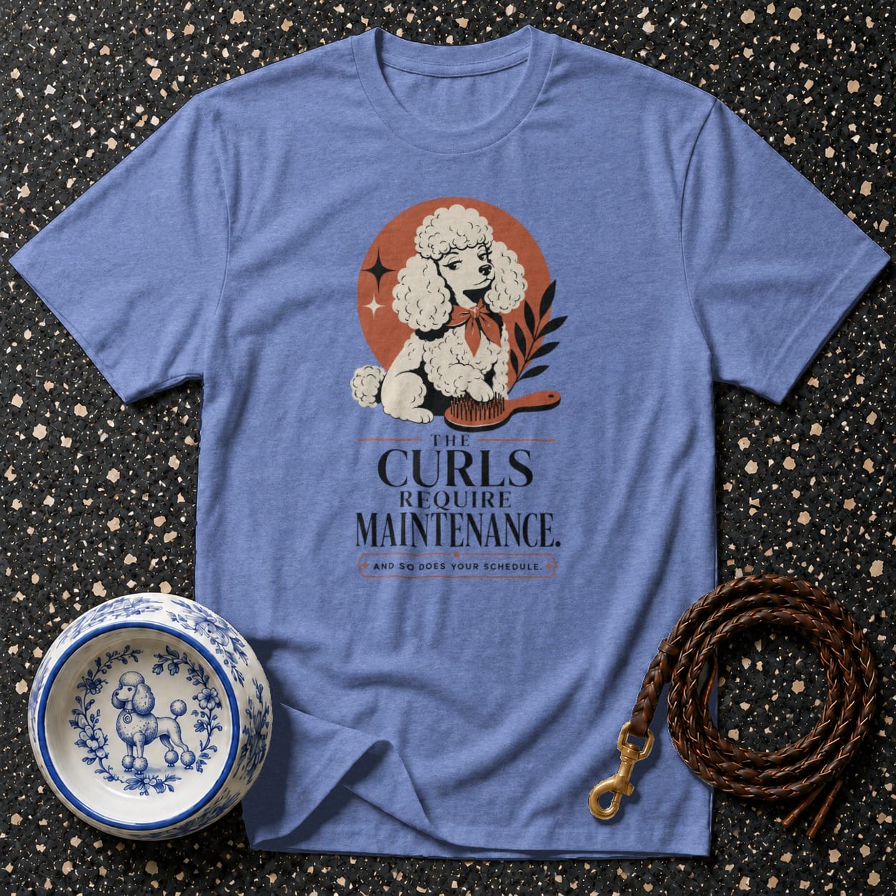 Blue t-shirt with graphic of a poodle, brush, and text "The Curls Require Maintenance."