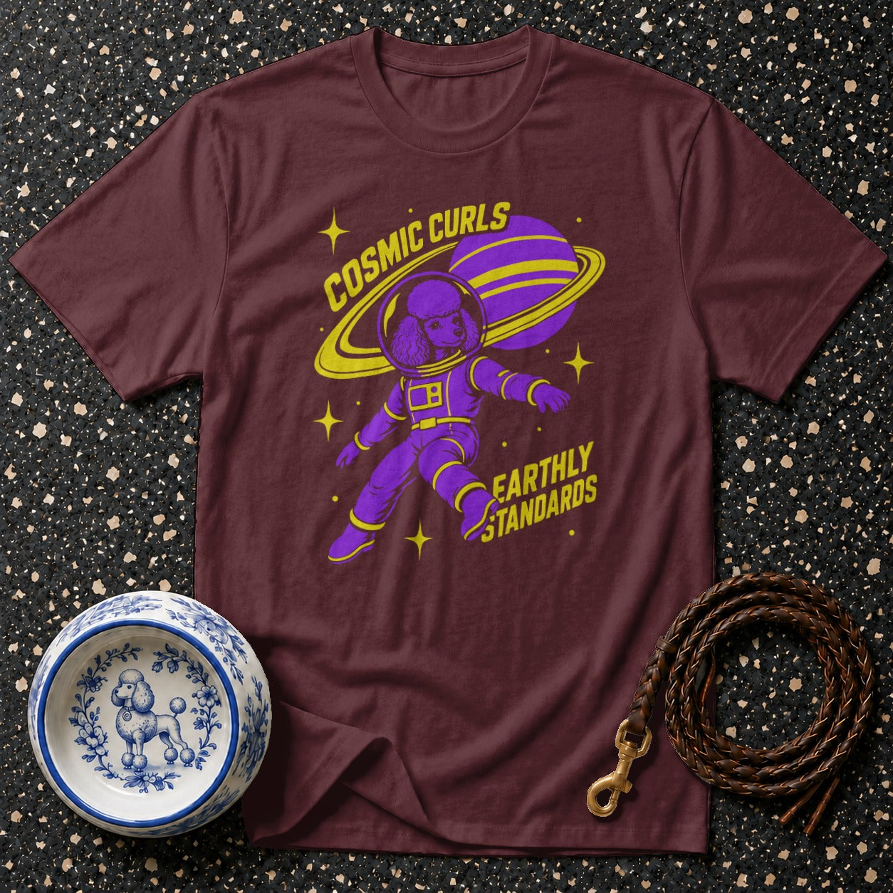 Maroon t-shirt with a purple poodle astronaut graphic and yellow text "COSMIC CURLS" and "EARTHLY STANDARDS".