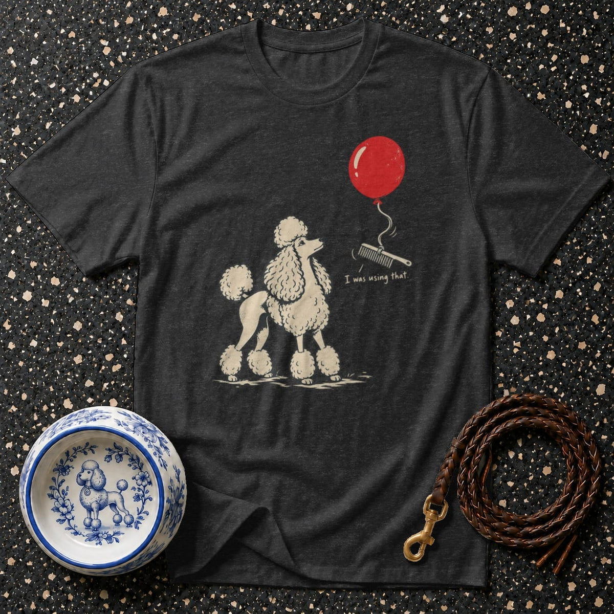 Dark t-shirt with graphic of a poodle, red balloon, comb, and text "I was using that."