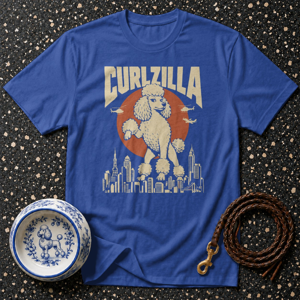Blue t-shirt with a graphic of a poodle towering over a city skyline with "CURLZILLA" text.