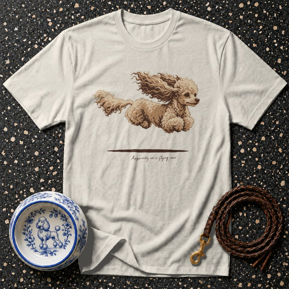Light beige t-shirt with a flying poodle graphic and text "Apparently we're flying now".