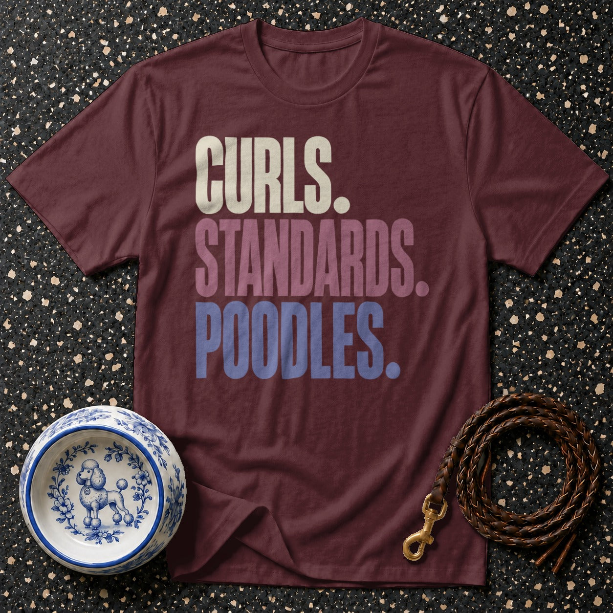 Maroon t-shirt with text "Curls. Standards. Poodles." next to a dog bowl and leash.