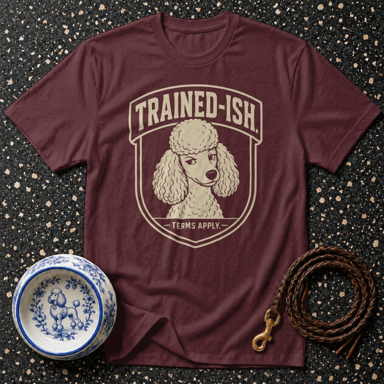 Maroon t-shirt with a poodle graphic that reads "TRAINED-ISH - TERMS APPLY."