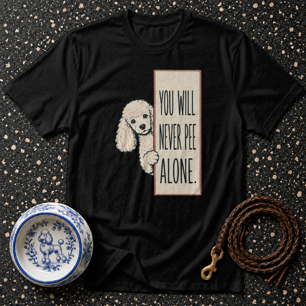 Black t-shirt with a cream rectangle featuring a poodle and text: "YOU WILL NEVER PEE ALONE."