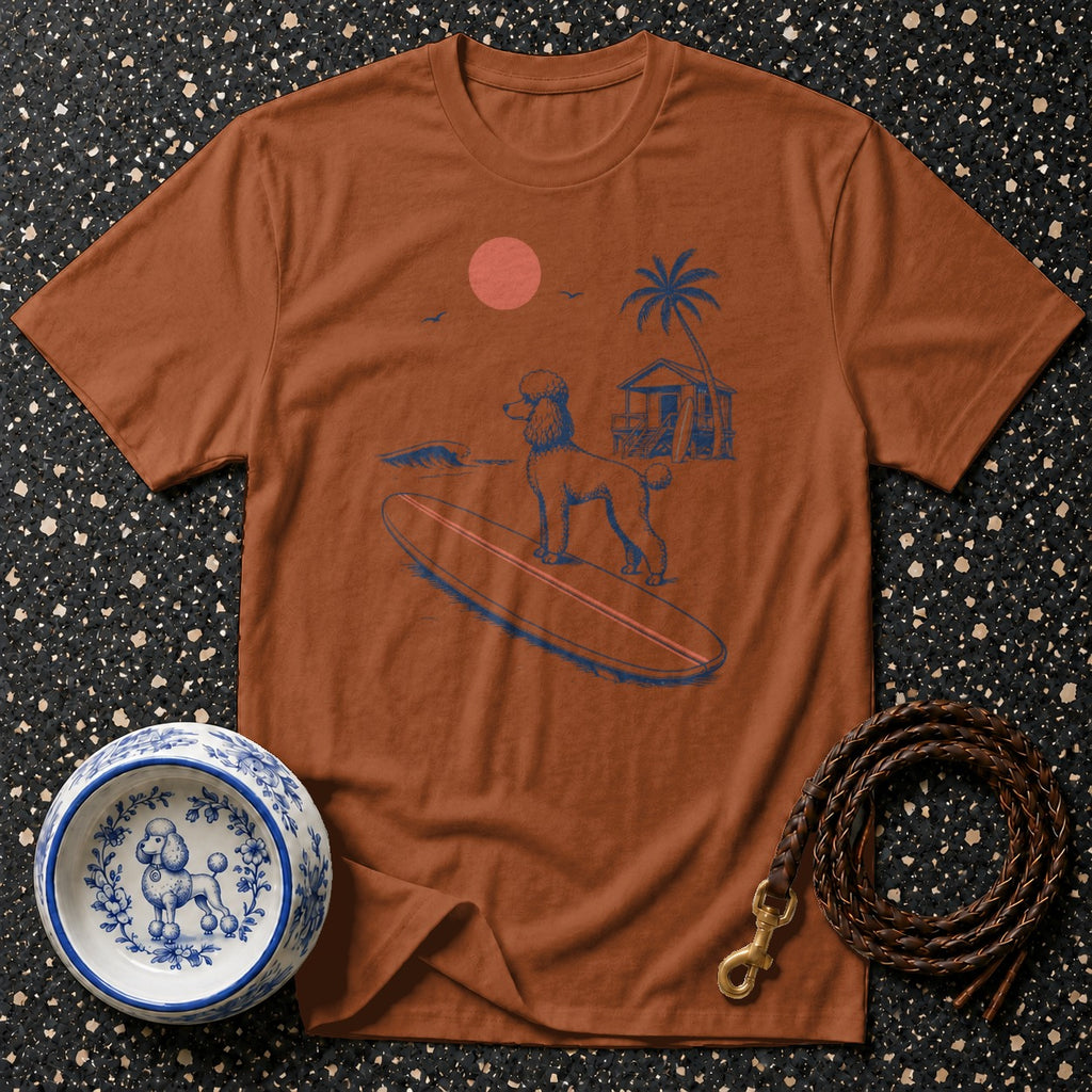 Brown t-shirt with a blue graphic of a poodle surfing near a beach hut.