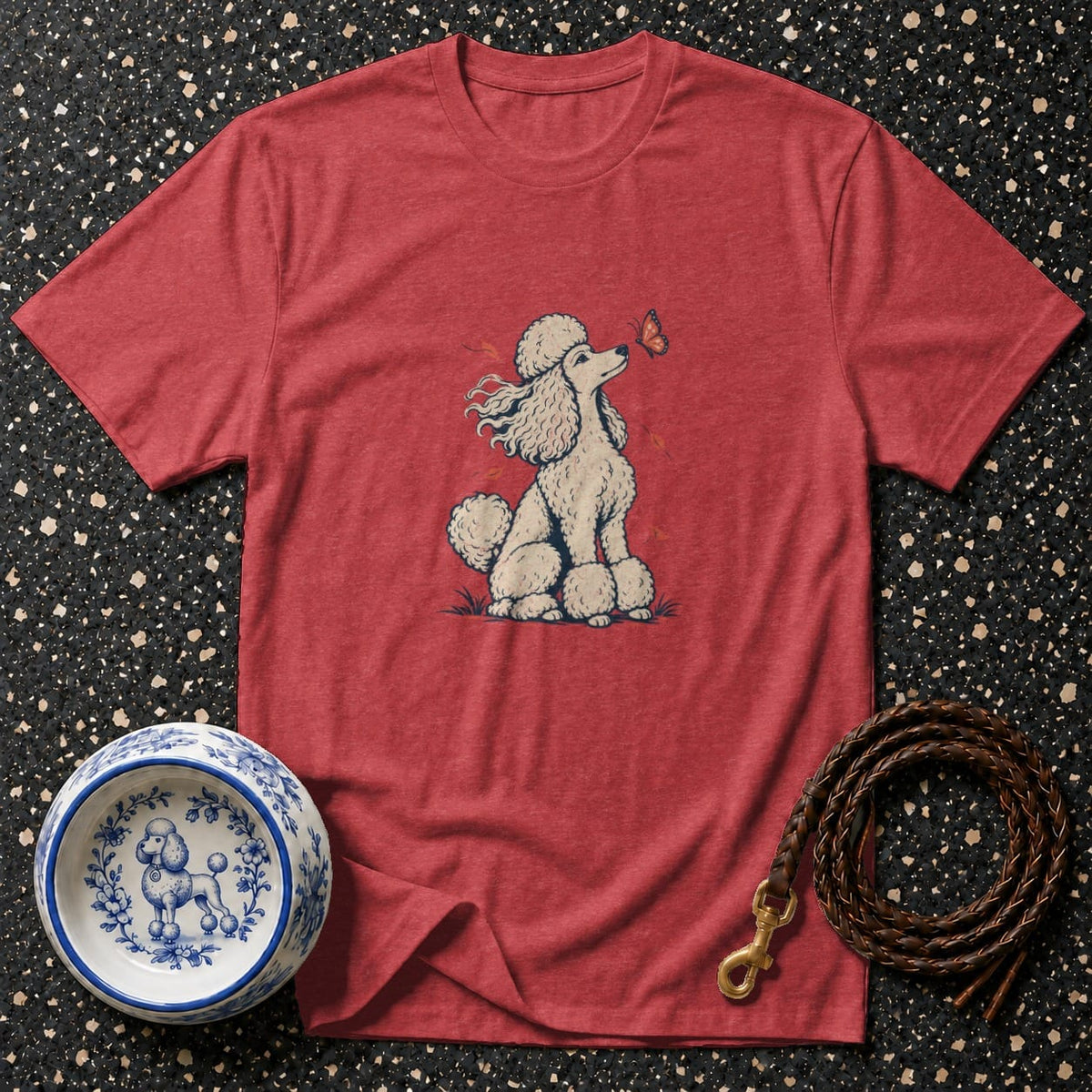 Red t-shirt with a white poodle and butterfly graphic, next to a blue and white poodle bowl and leash.