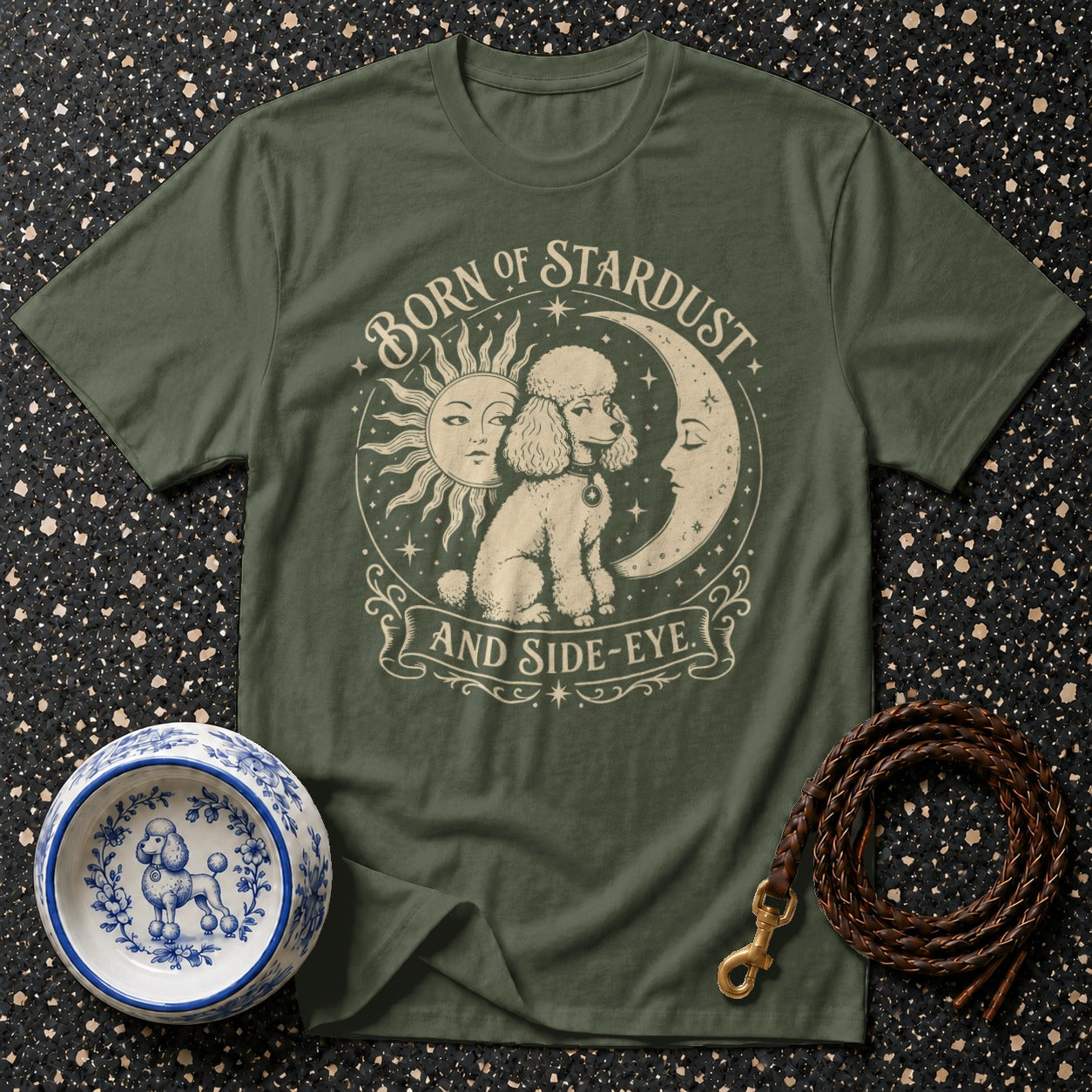 Green t-shirt with poodle, sun, and moon design reading "Born of Stardust and Side-Eye."