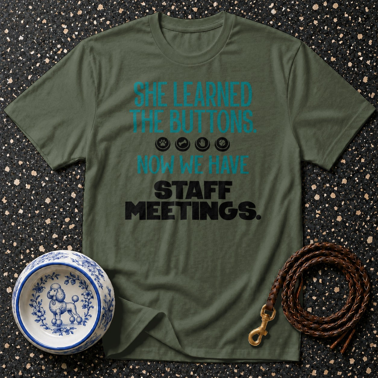 Olive green t-shirt with "She learned the buttons. Now we have staff meetings" text.