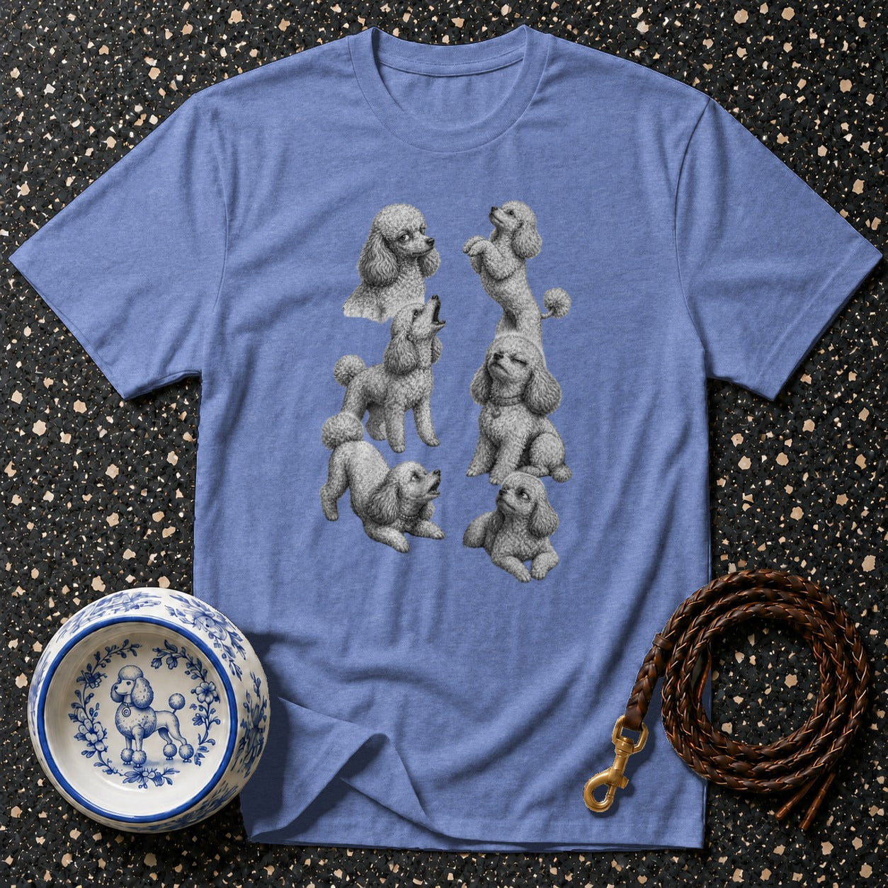 Light blue t-shirt with multiple grey poodle illustrations, next to a decorative dog bowl and leash.