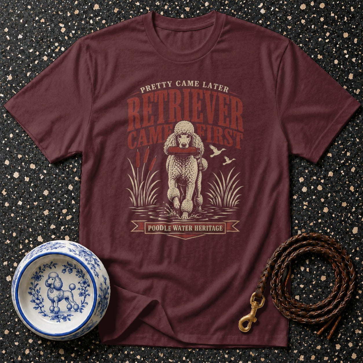 Maroon t-shirt with a poodle retrieving a stick and text "PRETTY CAME LATER RETRIEVER CAME FIRST POODLE WATER HERITAGE".
