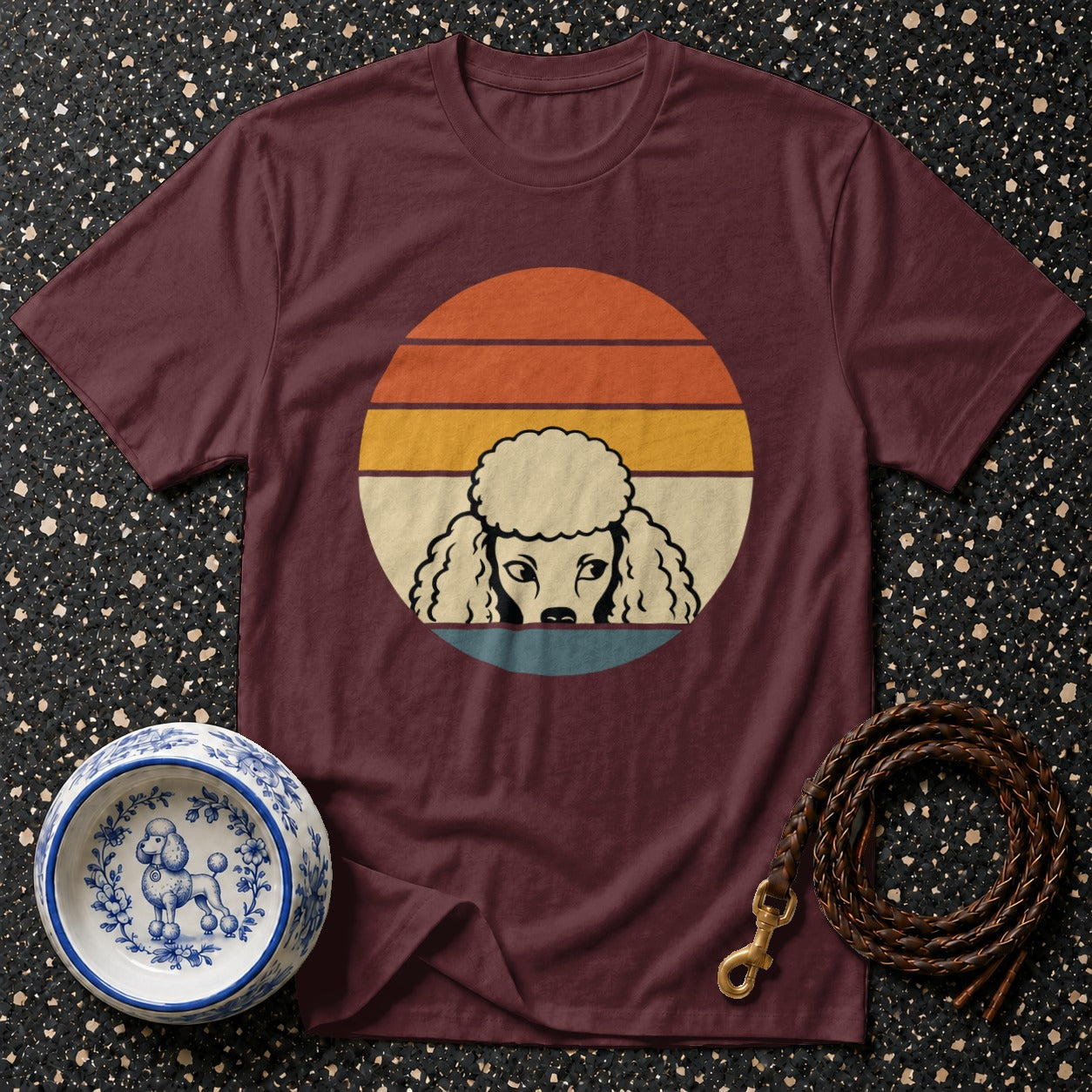 Maroon t-shirt with retro poodle graphic in a sun circle, a decorative dog bowl, and leash.