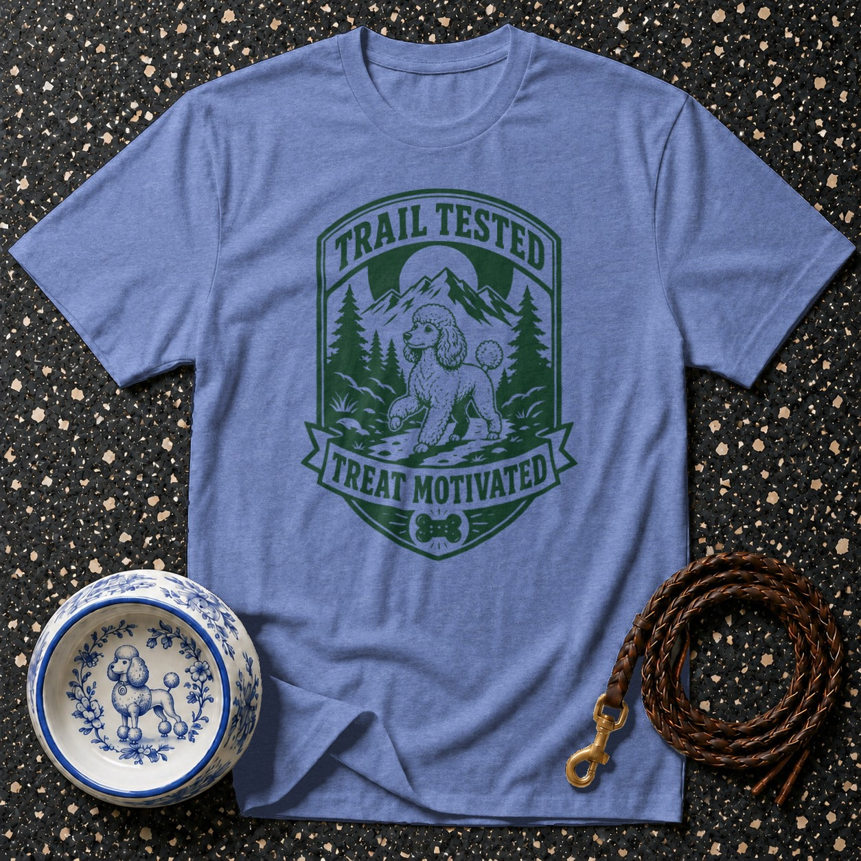 Light blue t-shirt with green graphic of poodle, mountains, trees, and text "TRAIL TESTED TREAT MOTIVATED".