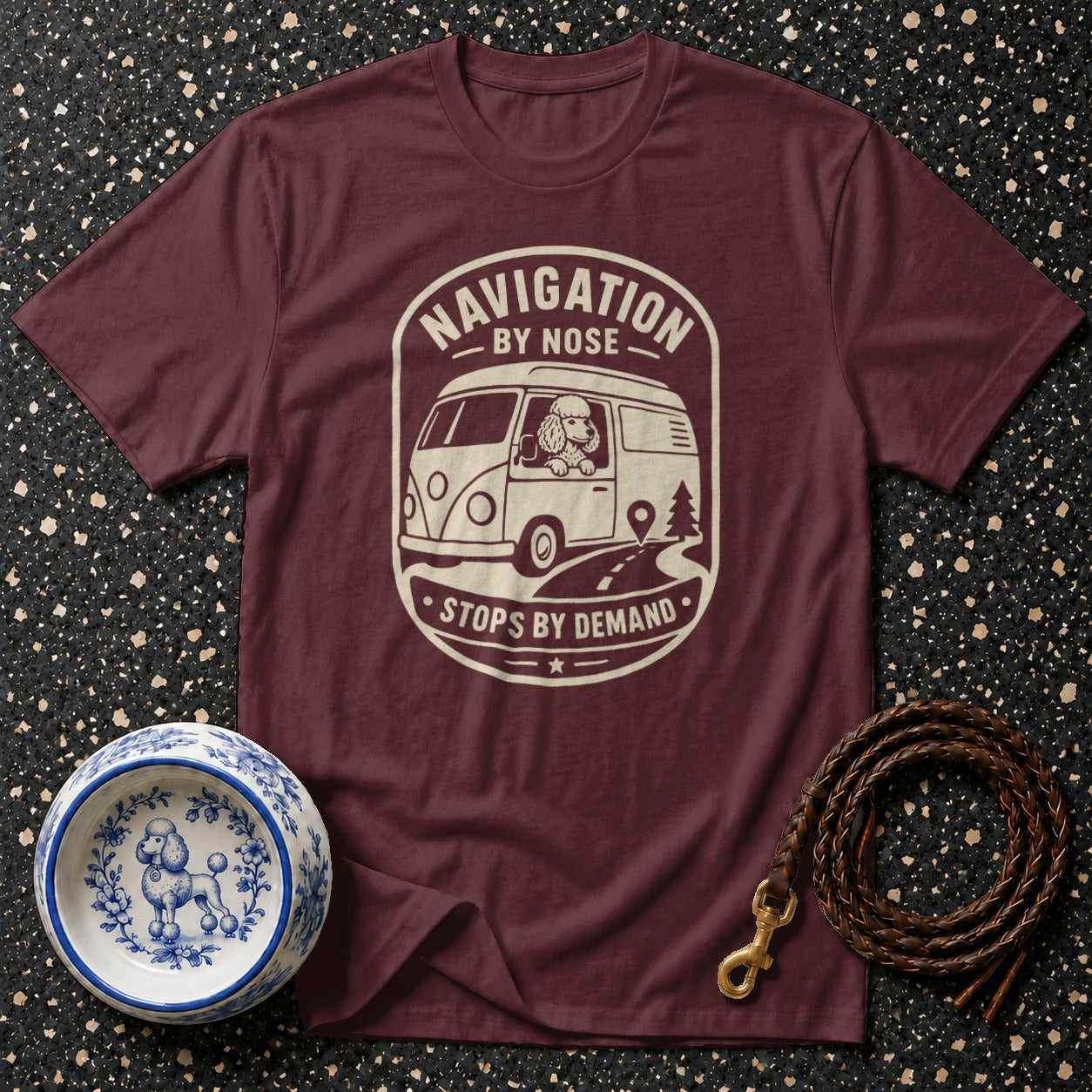 Maroon t-shirt with graphic of poodle driving camper van, text "Navigation by Nose Stops by Demand".