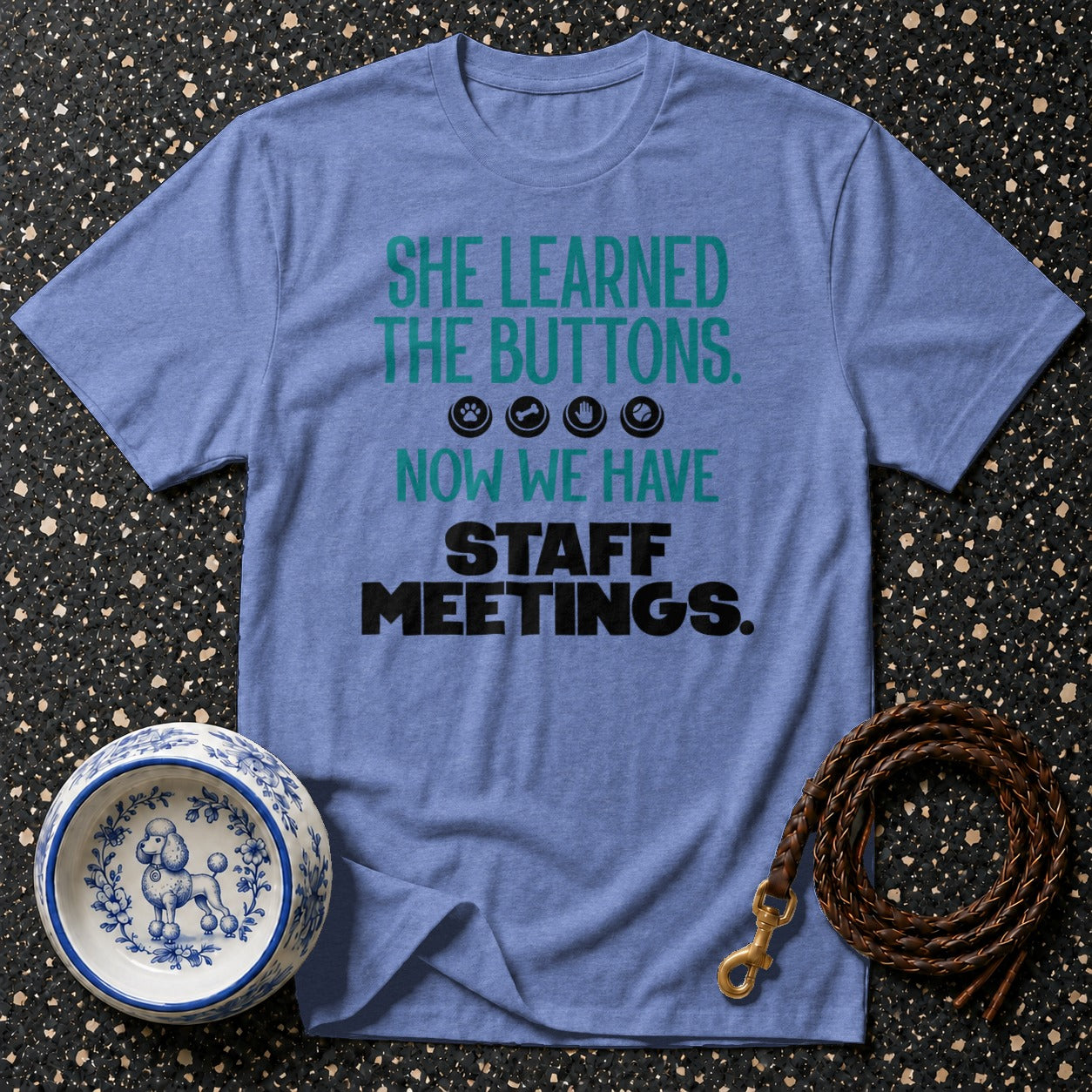 Blue t-shirt with text "SHE LEARNED THE BUTTONS. NOW WE HAVE STAFF MEETINGS."