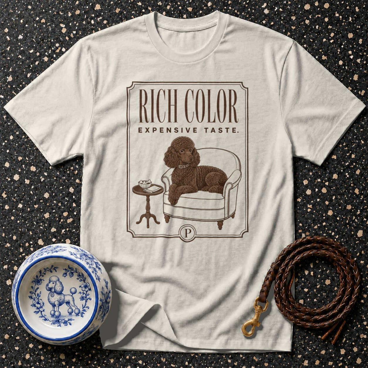T-shirt with a brown poodle lounging in a chair, text "RICH COLOR EXPENSIVE TASTE."