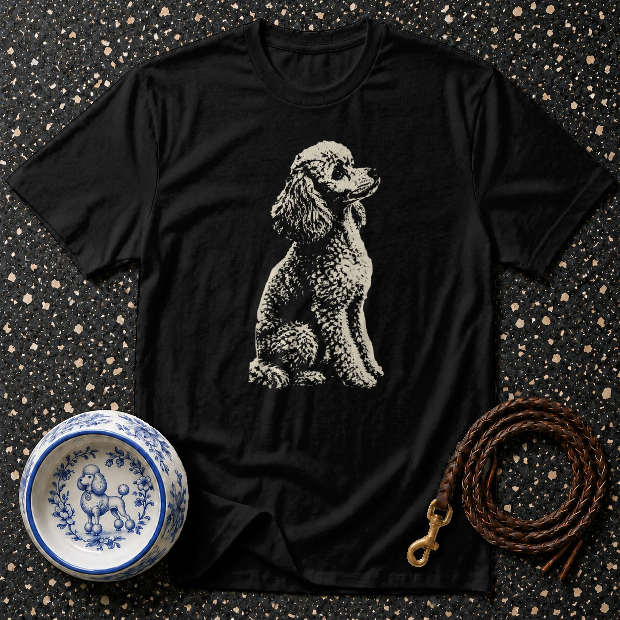 Black t-shirt with seated poodle graphic, blue and white dog bowl, and brown leather leash.