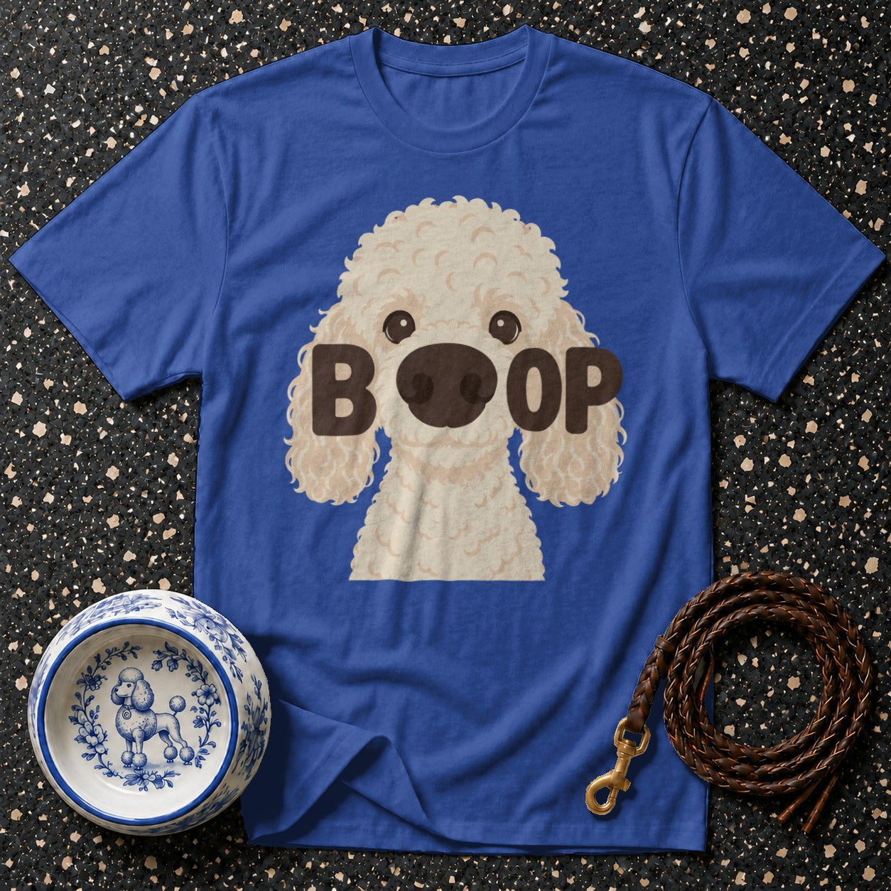 Blue t-shirt with cartoon poodle graphic and "BOOP" text, next to dog bowl and leash.