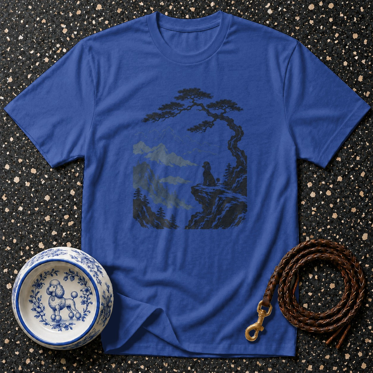 Blue t-shirt with dark graphic of dog on cliff overlooking mountains and dog bowl.
