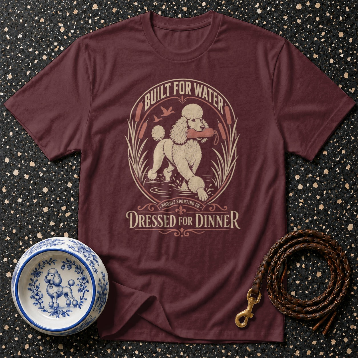 Maroon t-shirt with a graphic of a poodle retrieving a toy in water, text "BUILT FOR WATER" and "DRESSED FOR DINNER".
