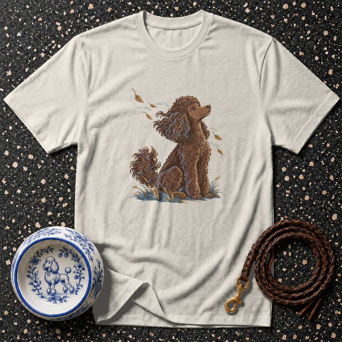 Light t-shirt with a brown poodle illustration, a decorative dog bowl, and a leather leash.