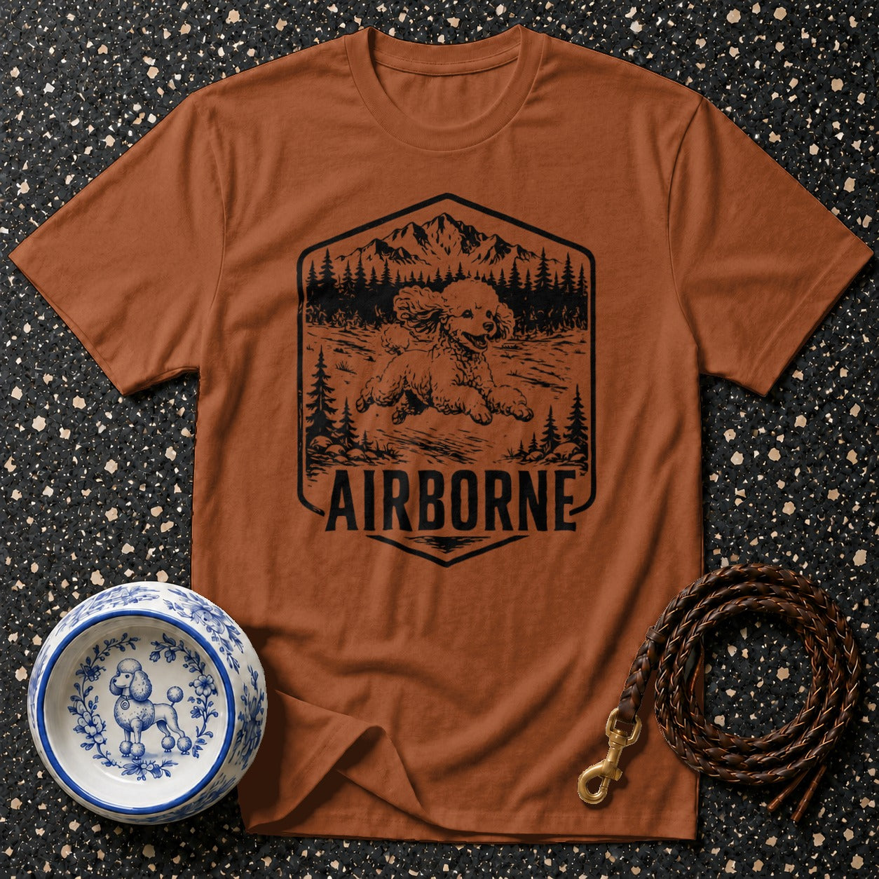 Brown t-shirt with a black graphic of a poodle in the mountains with "AIRBORNE" text.