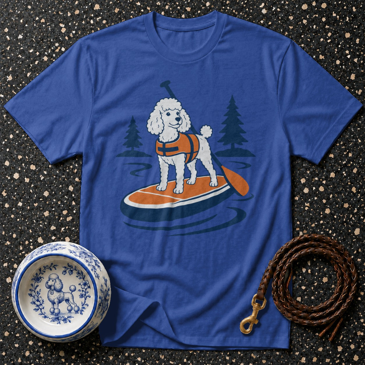 Blue t-shirt with illustration of poodle on paddleboard with life vest and trees.