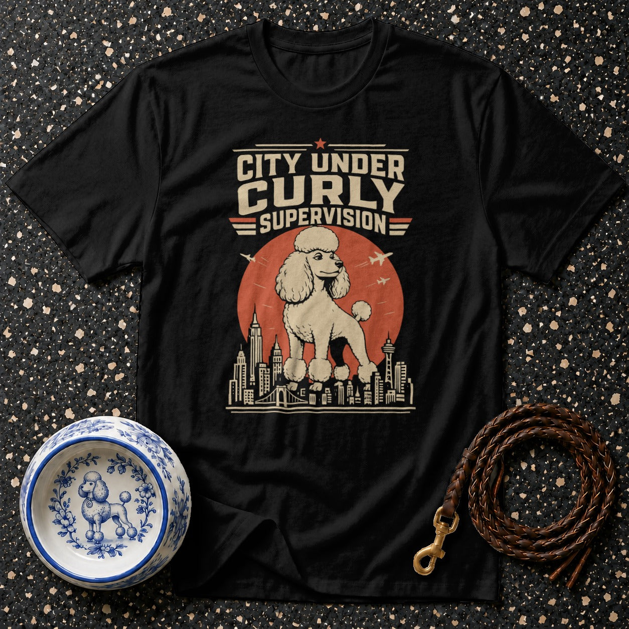 Black t-shirt with a poodle standing on city buildings under text "CITY UNDER CURLY SUPERVISION".