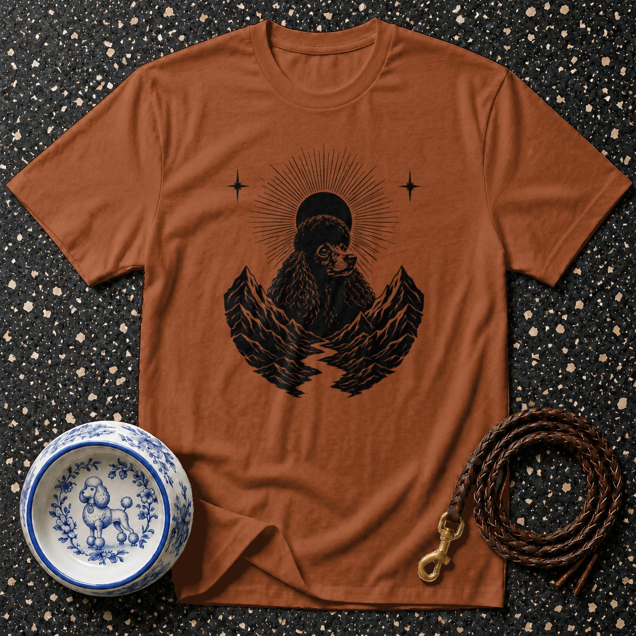 Brown t-shirt with black poodle and mountain graphic, dog bowl, and leather leash.