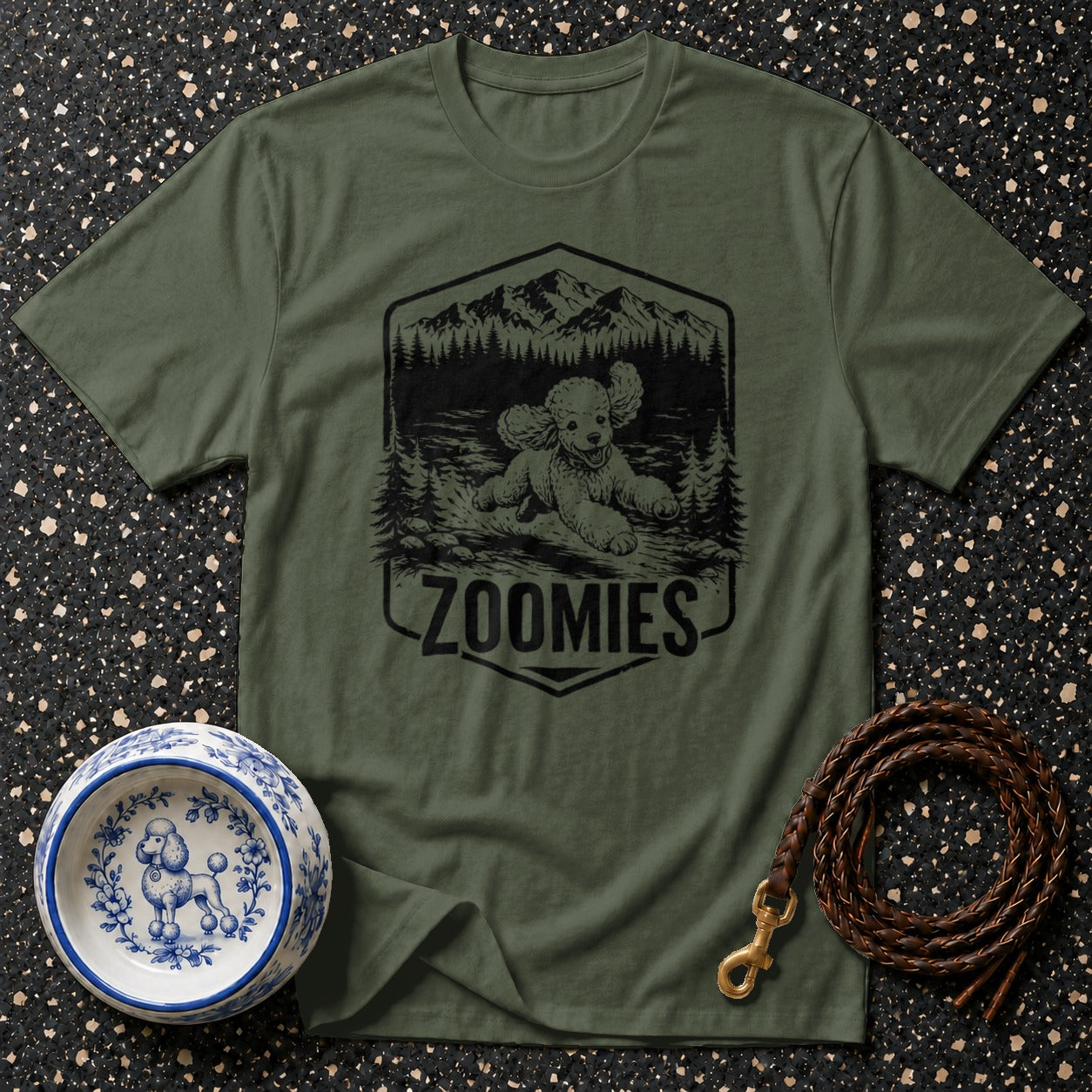 Olive green t-shirt with a black graphic of a poodle running in the mountains, text "ZOOMIES" below.