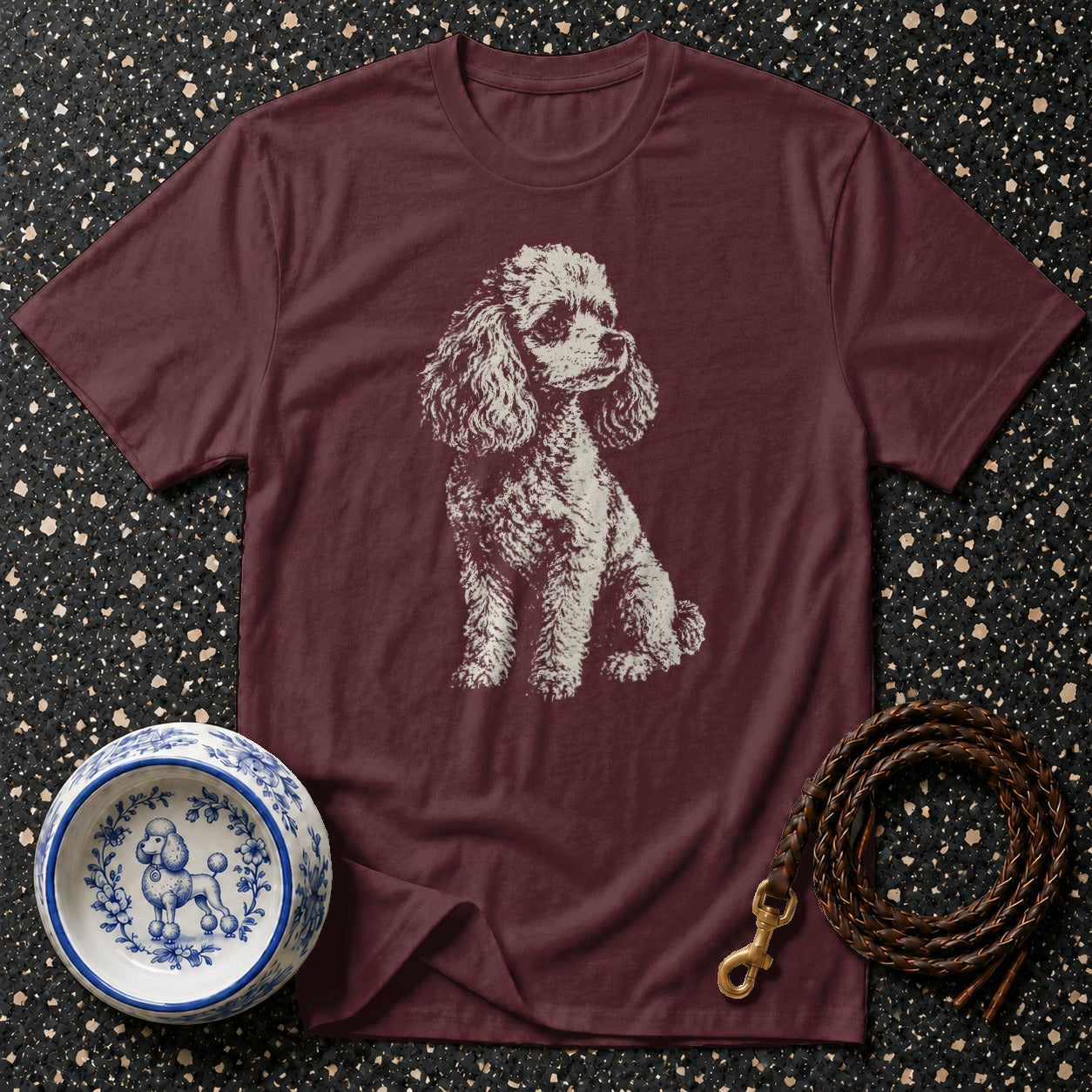 Maroon t-shirt with white poodle graphic, a blue and white dog bowl, and a leather leash.