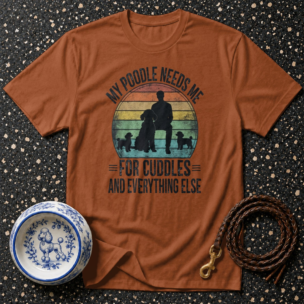 Brown t-shirt with a graphic of a person and poodles with text "MY POODLE NEEDS ME FOR CUDDLES AND EVERYTHING ELSE."
