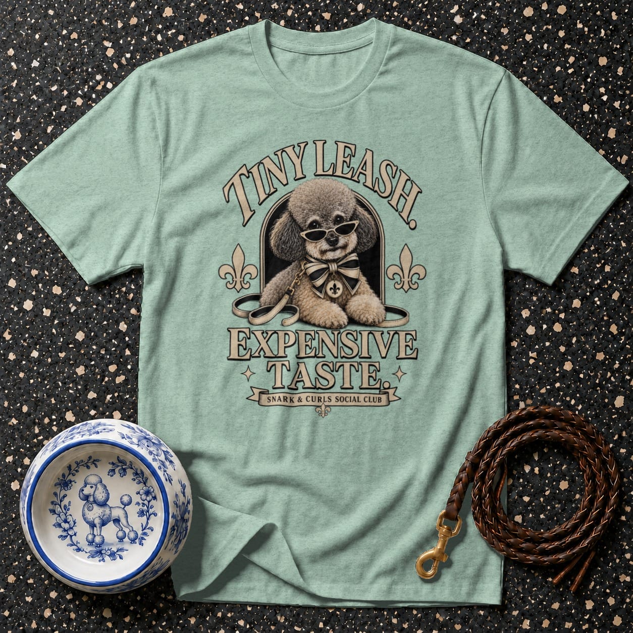 Light teal t-shirt with a poodle wearing sunglasses and a bow tie, text reads "Tiny Leash Expensive Taste."