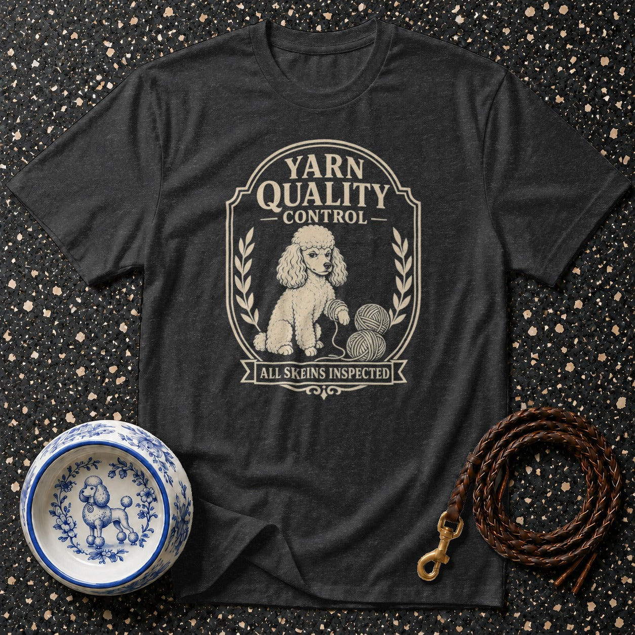 A poodle sits with yarn skeins on a dark t-shirt with "Yarn Quality Control" text.