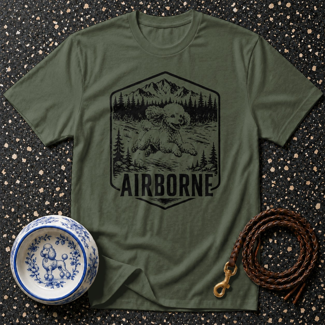 Green t-shirt with black graphic of poodle jumping in mountain landscape and "AIRBORNE" text.