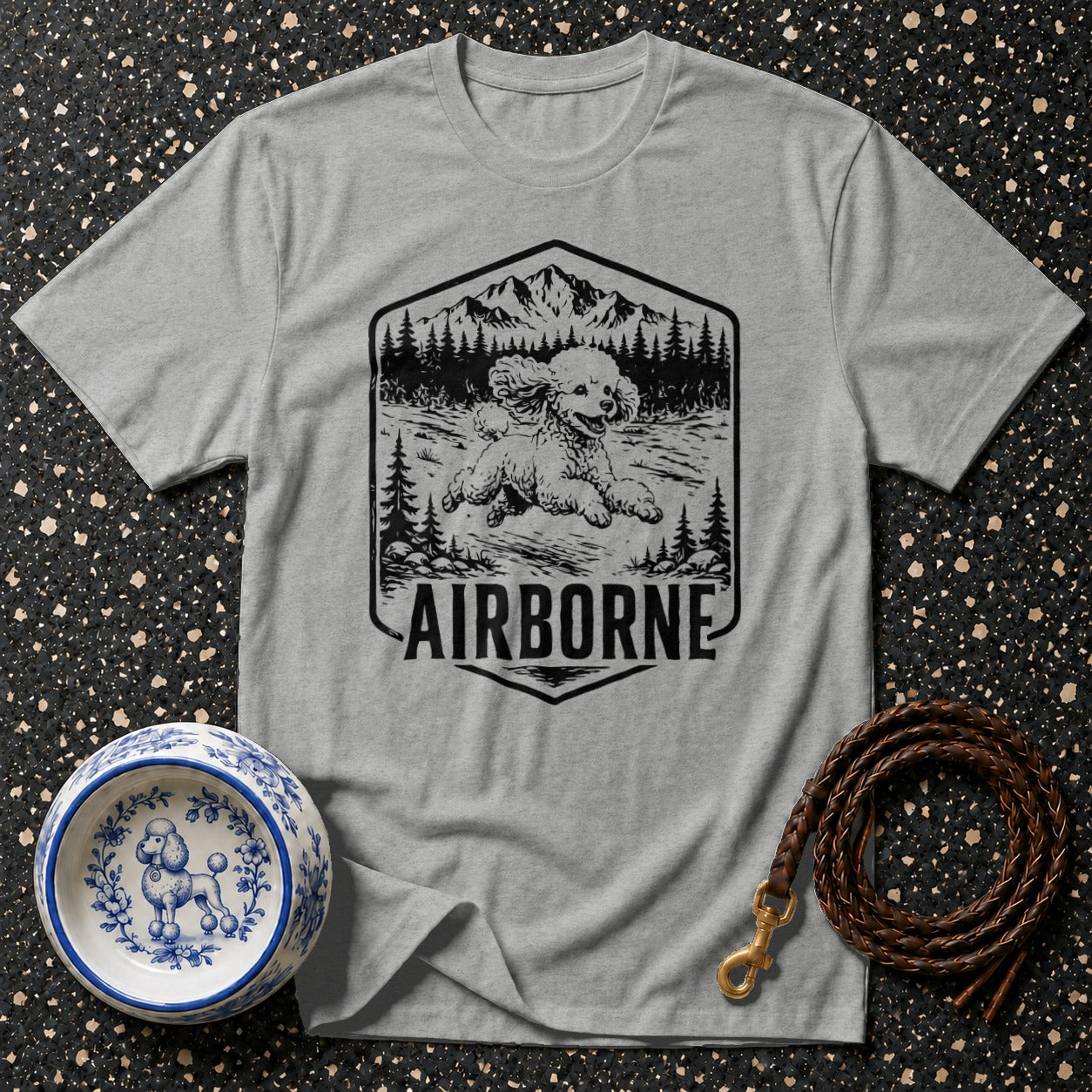 Grey t-shirt with a graphic of a poodle running in a forest, mountains, and the word AIRBORNE.
