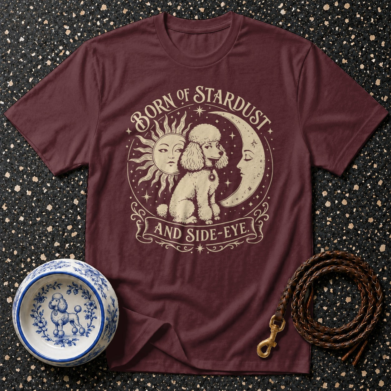 Maroon t-shirt with poodle, sun, moon, and text "BORN OF STARDUST AND SIDE-EYE".