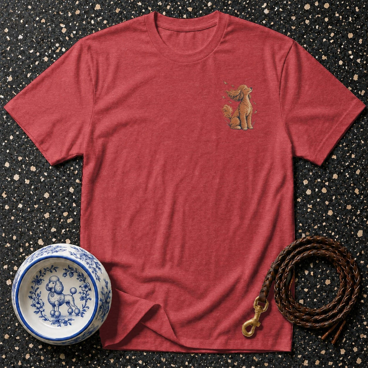 Red t-shirt with embroidered poodle graphic, dog bowl, and leash on speckled background.
