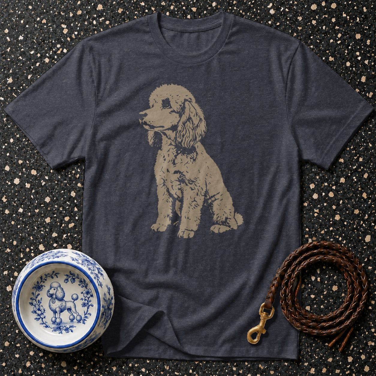 Dark gray t-shirt with a beige poodle graphic, beside a decorative dog bowl and leash.
