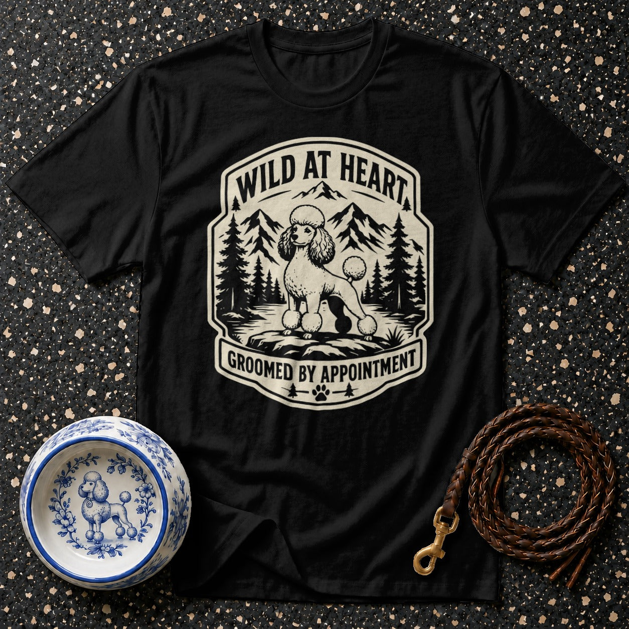 Black t-shirt with a vintage graphic of a poodle in a mountain landscape, reading "WILD AT HEART GROOMED BY APPOINTMENT".