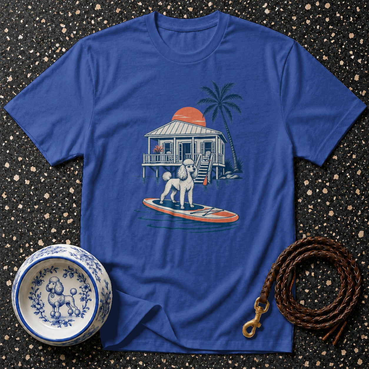 Blue t-shirt with a poodle on a paddleboard in front of a beach house.