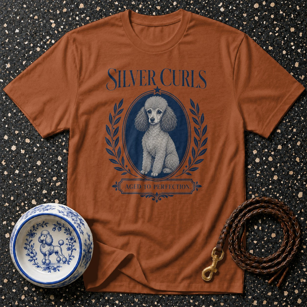 Brown t-shirt with "Silver Curls" and poodle graphic, next to a decorative dog bowl and leash.