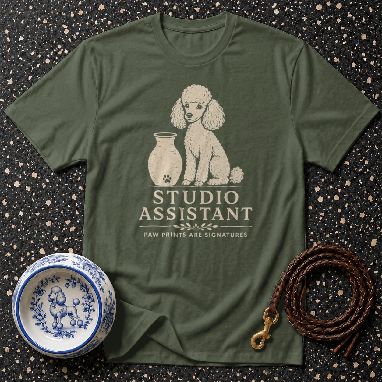 Olive green t-shirt with a poodle graphic and "STUDIO ASSISTANT" text.