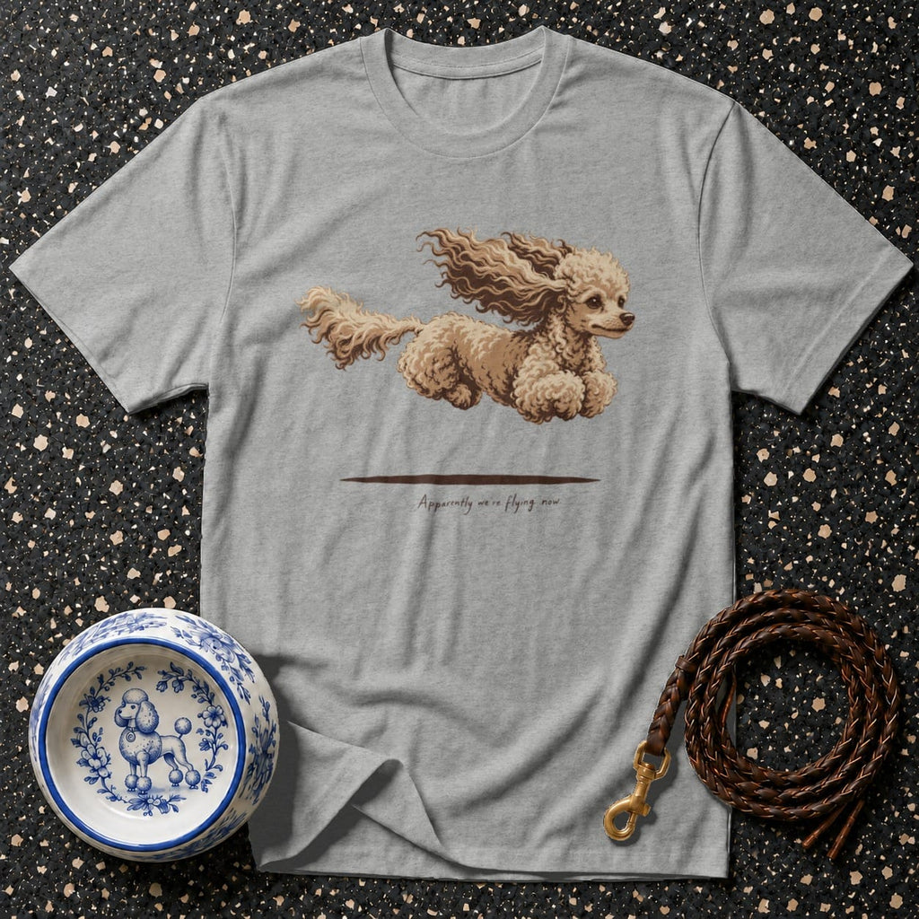 Grey t-shirt with a cartoon poodle mid-air and text "Apparently we're flying now".